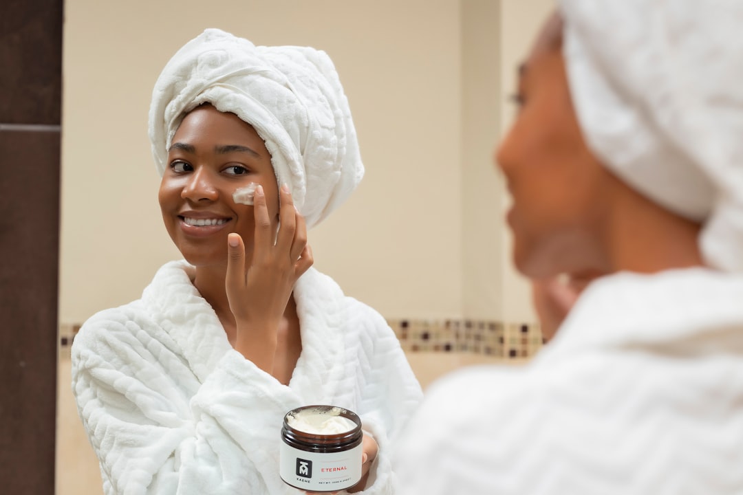 uma mulher com uma toalha na cabeça e um pote de creme no rosto